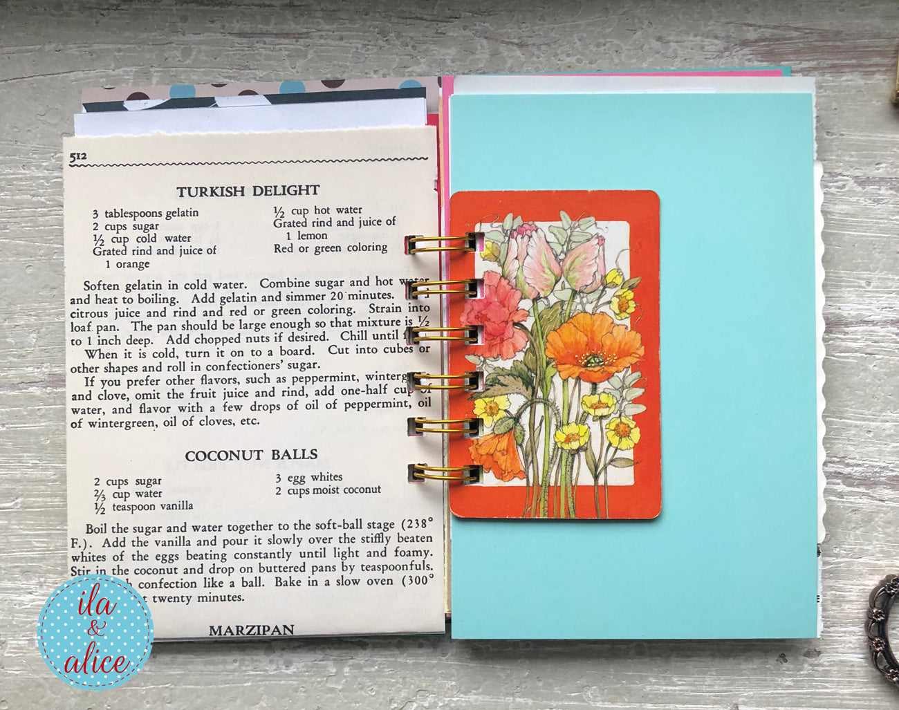 Open book with recipe pages and a floral bookmark on a wooden surface