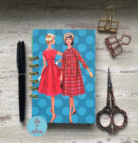 Notebook with vintage-style illustration of two women on a blue polka dot background, surrounded by office supplies.