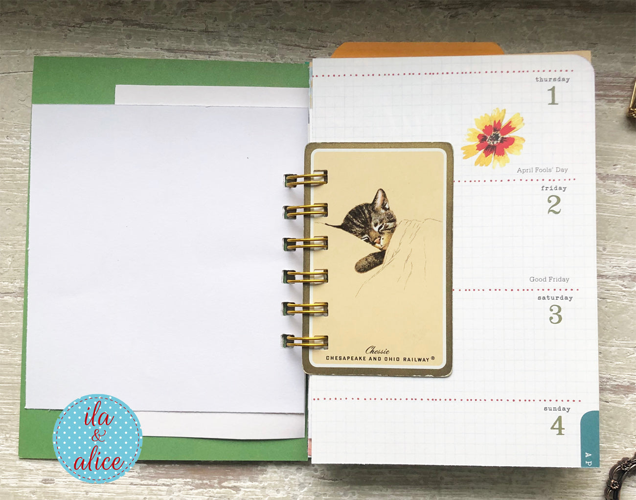 Open planner with a cat illustration on a wooden surface, featuring the brand 'ila & alice'.