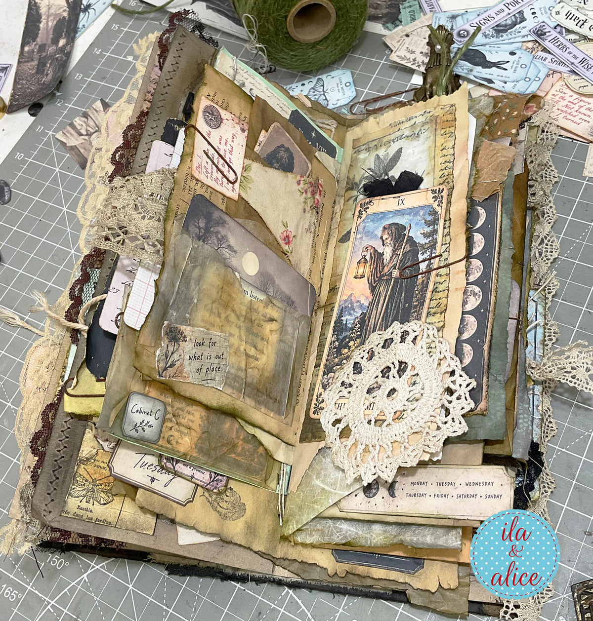 Heavily layered witch’s journal with a moonlit Hermit card, translucent pocket, handwritten notes, antique lace and aged paper ephemera.